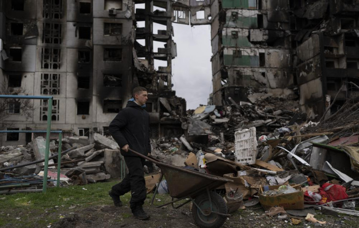 A young man pushes a wheelbarrow in front of a destroyed apartment building in the town of Borodyanka, Ukraine, on Sunday, April 10, 2022.