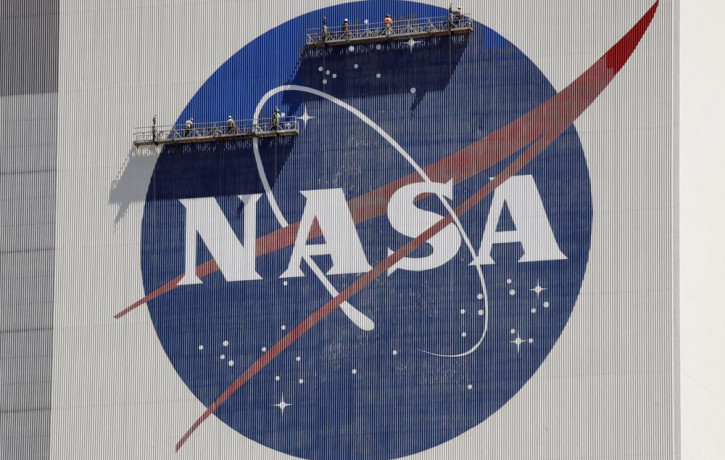 FILE - Workers on scaffolding repaint the NASA logo near the top of the Vehicle Assembly Building at the Kennedy Space Center in Cape Canaveral, Florida, Wednesday, May 20, 2020.