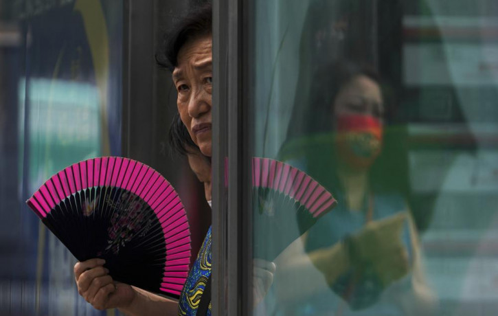 A woman fans herself at an advertisement boards on a bus stand reflecting a masked commuter as they wait for buses in Beijing, Tuesday, July 5, 2022. AP/RSS Photo