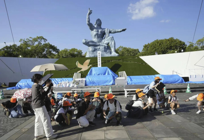 Visitors to the Peace Park crouch as an earthquake alert was issued in Nagasaki, western Japan, Thursday, Aug. 8, 2024. (Kyodo News via AP)