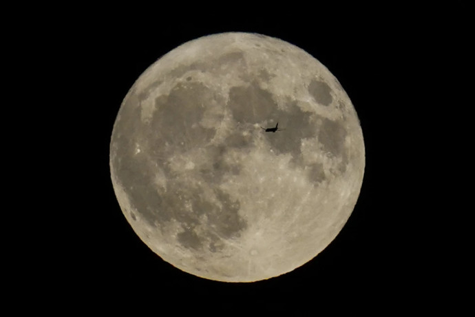 FILE - A plane passes in front of the moon, Aug. 30, 2023, in Chicago. Scientists have confirmed a cave on the moon, not far from where Neil Armstrong and Buzz Aldrin landed 55 years ago this week, and suspect there are hundreds more that could house future astronauts. AP/RSS Photo